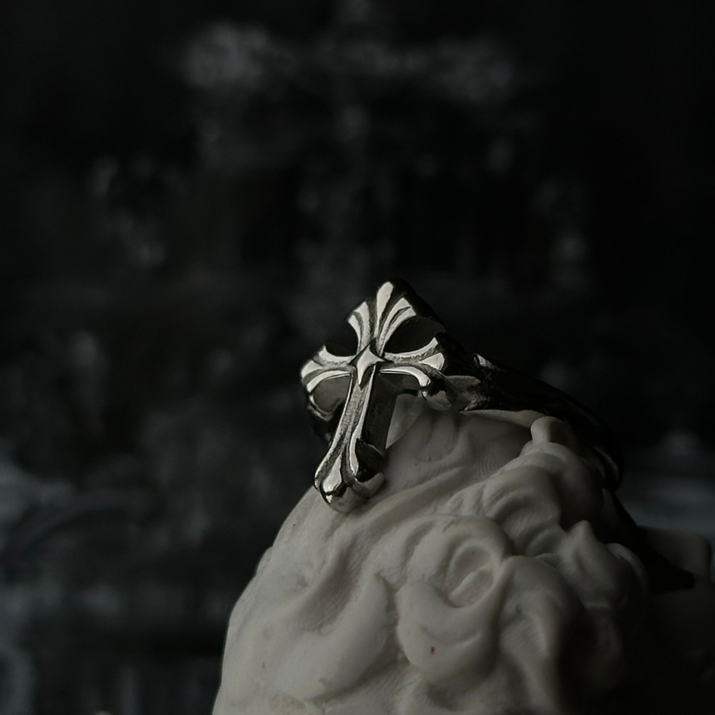 Anillo de acero inoxidable 'Follow Ring Lil Cross' con diseño de cruz en relieve, de la marca Follow God, exhibido sobre una figura decorativa blanca