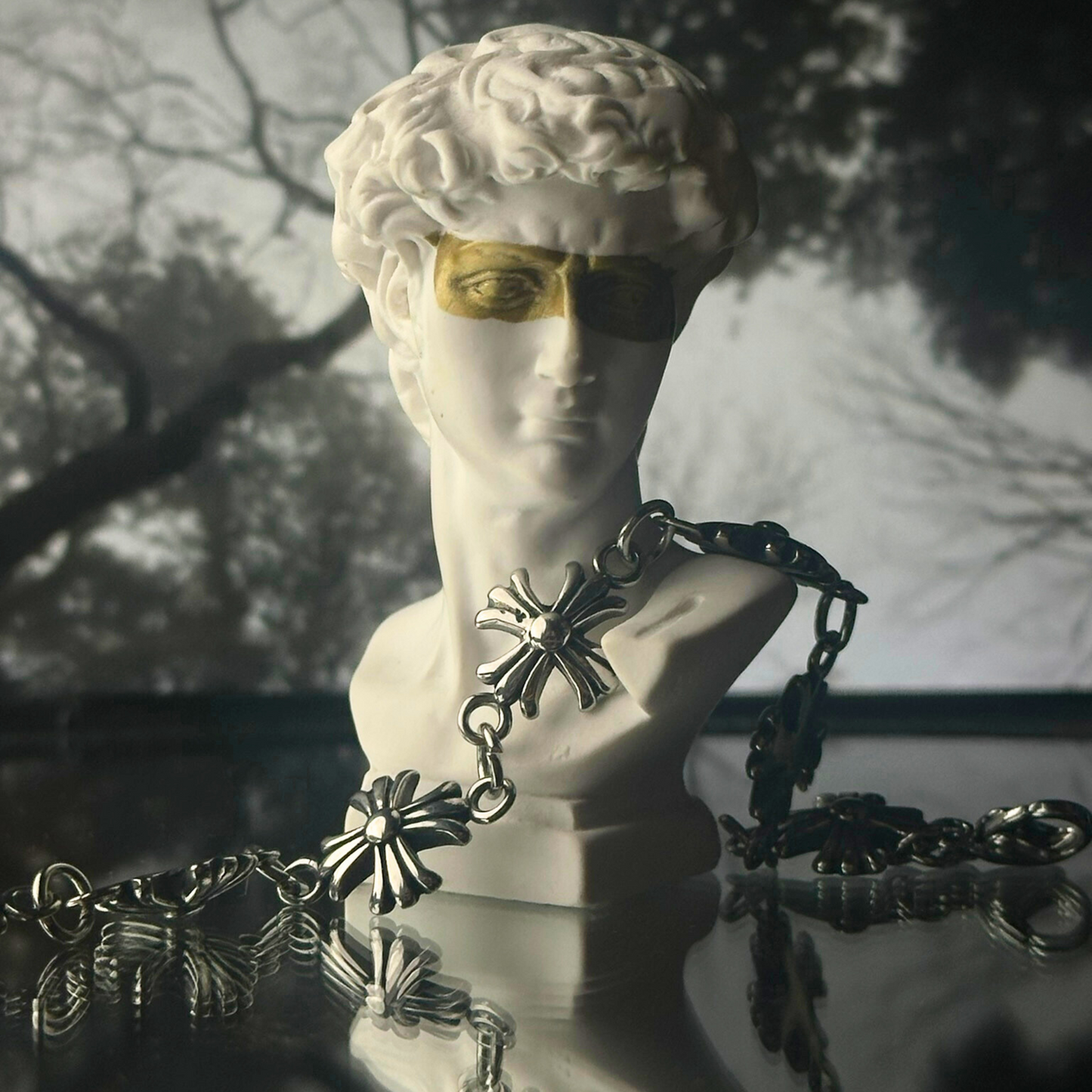 Pulsera de acero inoxidable 'Follow Bracelet' con diseño de cruces en relieve, de la marca Follow God, adornando una estatua blanca con venda dorada en los ojos