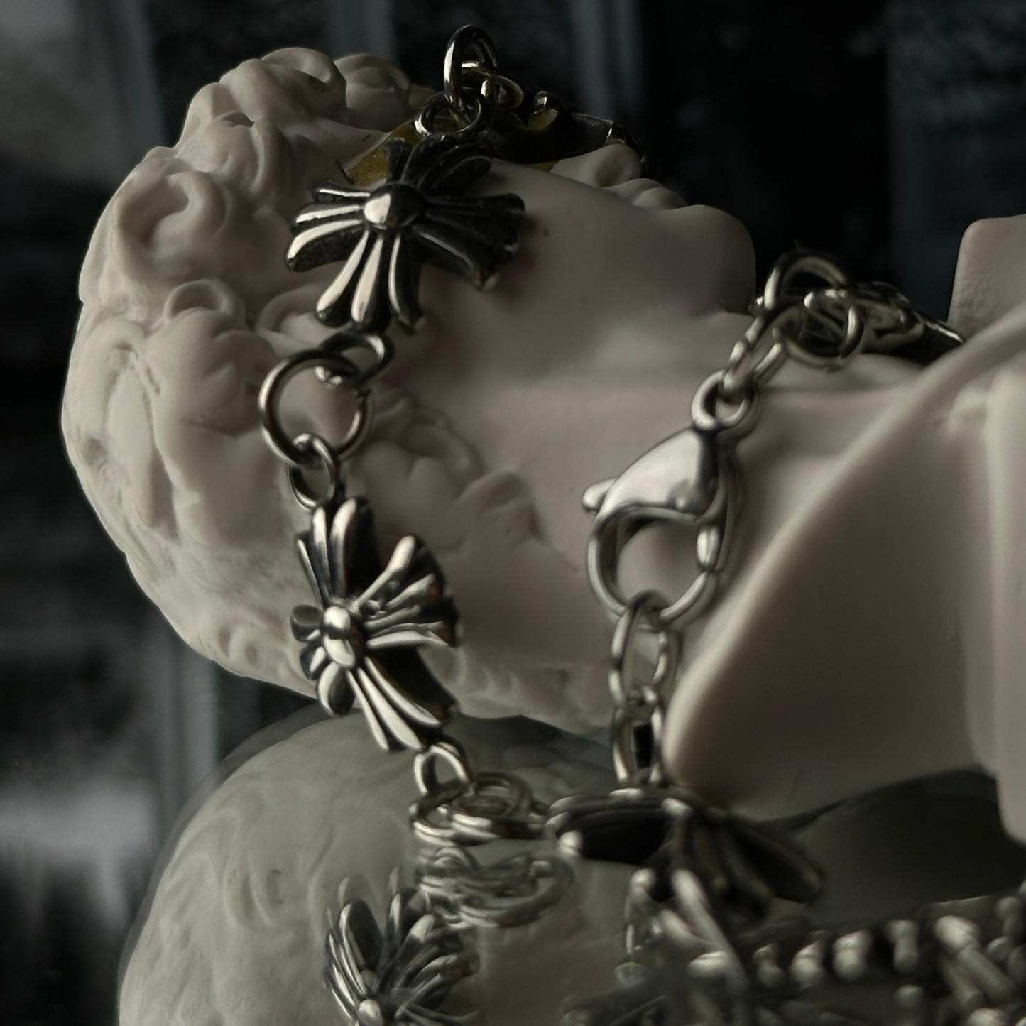 Detalle del cierre de la pulsera de acero inoxidable 'Follow Bracelet' con diseño de cruces en relieve, de la marca Follow God, exhibida sobre una figura decorativa blanca