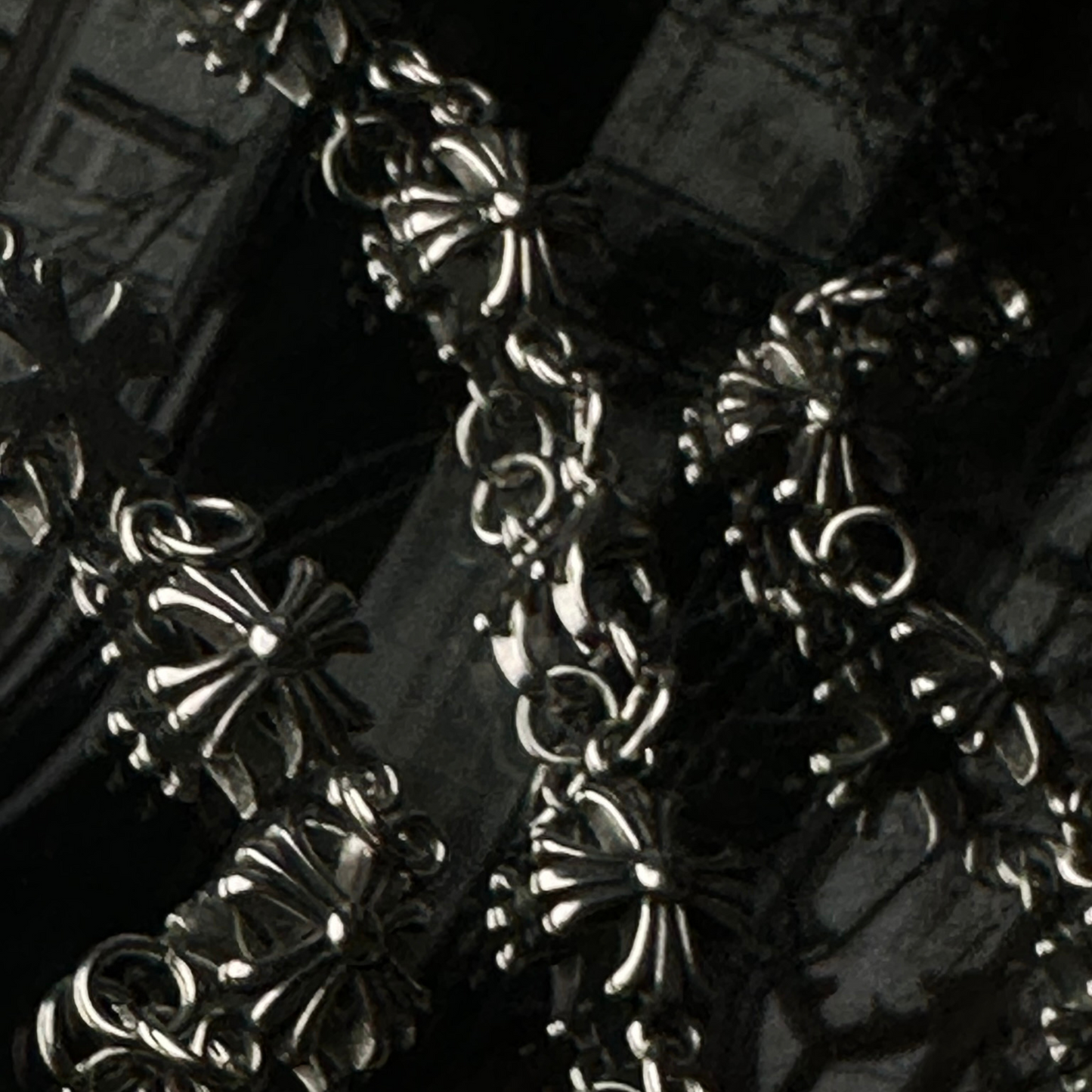 Detalle de varias pulseras de acero inoxidable 'Follow Bracelet' con diseño de cruces en relieve, de la marca Follow God, en un fondo oscuro