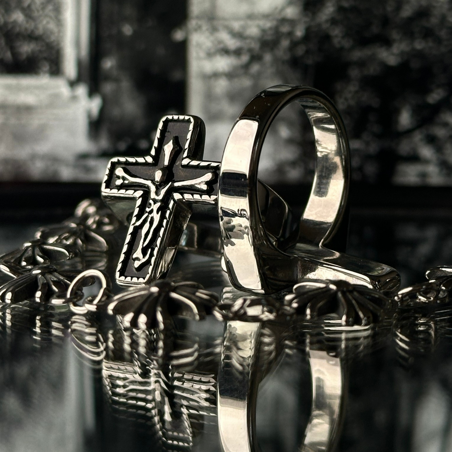 Dos vistas del anillo de acero inoxidable tipo sello 'Follow Ring Big Cross', acompañadas por la pulsera 'Follow Bracelet', de la marca Follow God, sobre una superficie reflectante